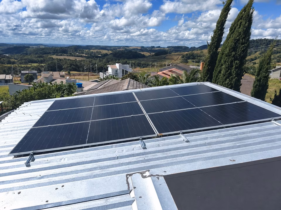 Módulos solares em telhado claro, com vista para a cidade e as colinas, em Barracão.