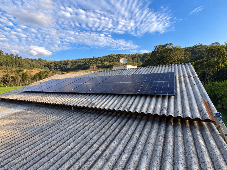 Painéis solares em telhado ondulado sob céu azul com nuvens, em Flor do Sertão.