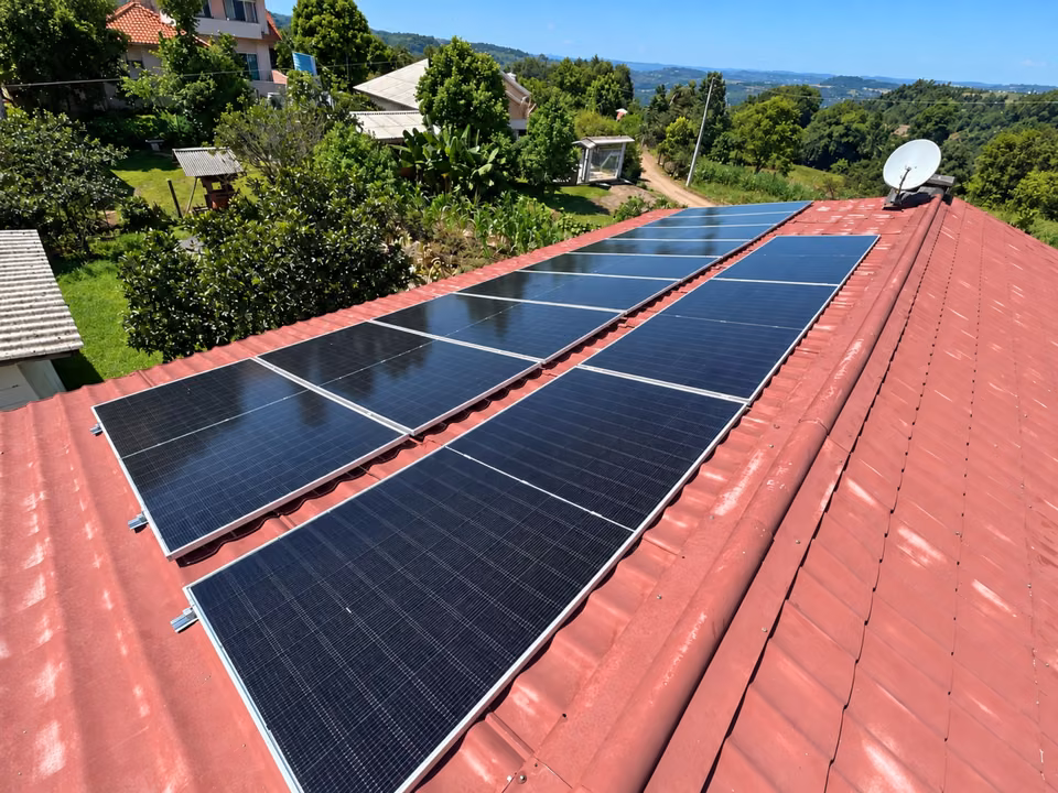 Fileiras de módulos solares sobre telhado vermelho, cercado por árvores, em Itapiranga.
