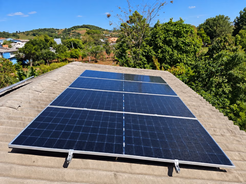Fileiras de módulos solares em telhado, com árvores ao redor, em Romelândia.