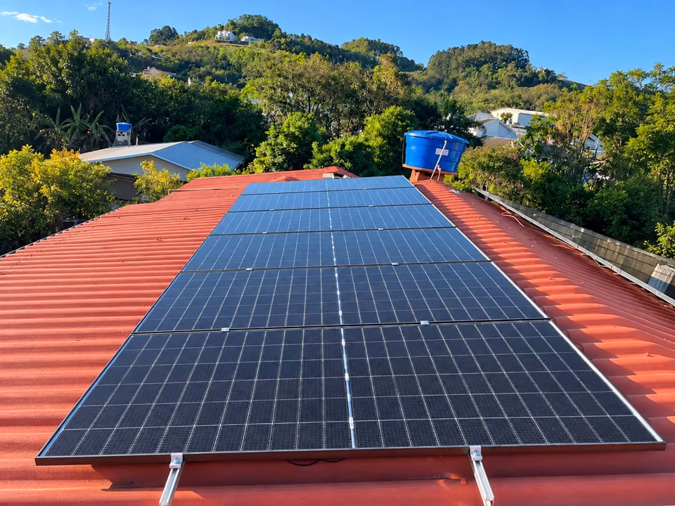 Módulos solares alinhados sobre telhado vermelho em uma área arborizada, em São José do Cedro.