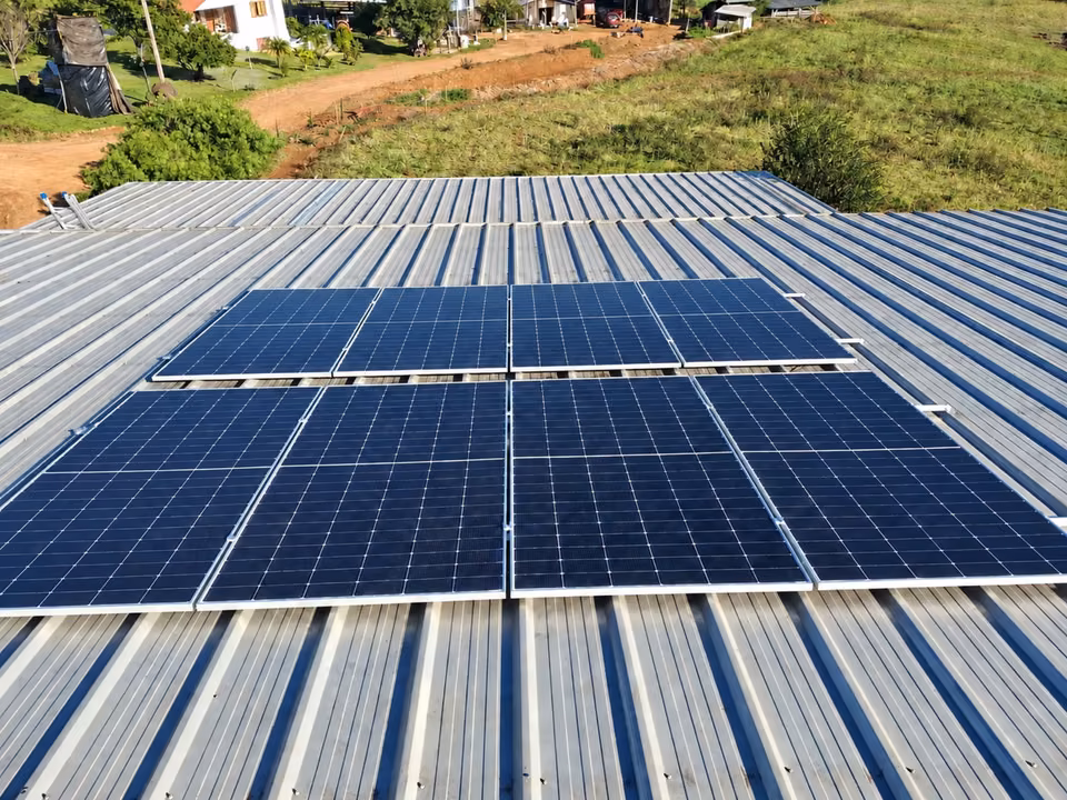 Módulos solares sobre cobertura metálica próxima a um terreno verde, em São Miguel do Oeste.