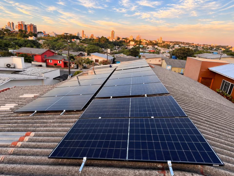 Módulos solares em telhado com a cidade ao fundo no fim da tarde, em São Miguel do Oeste.