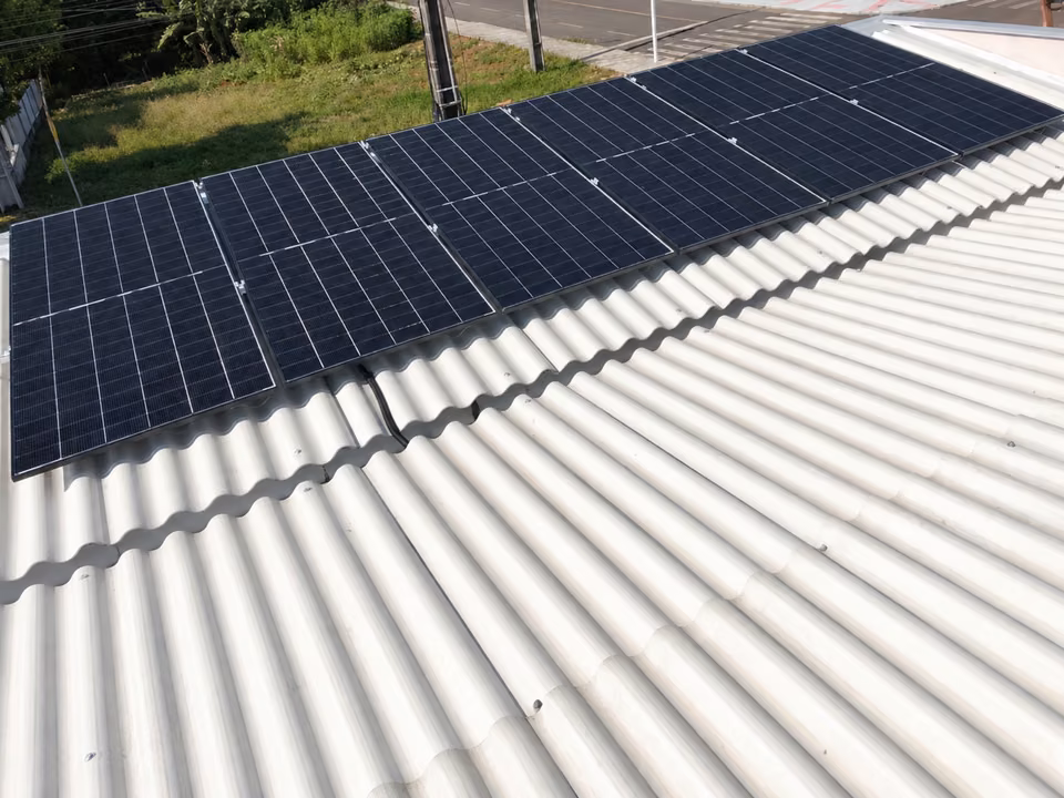 Conjunto de módulos solares sobre telhado claro em vista aérea, em São Miguel do Oeste.