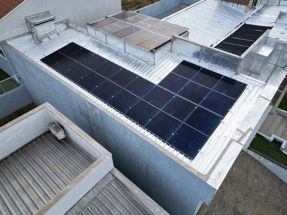 Vista aérea de módulos solares instalados em diferentes áreas de um telhado claro, em São Miguel do Oeste.
